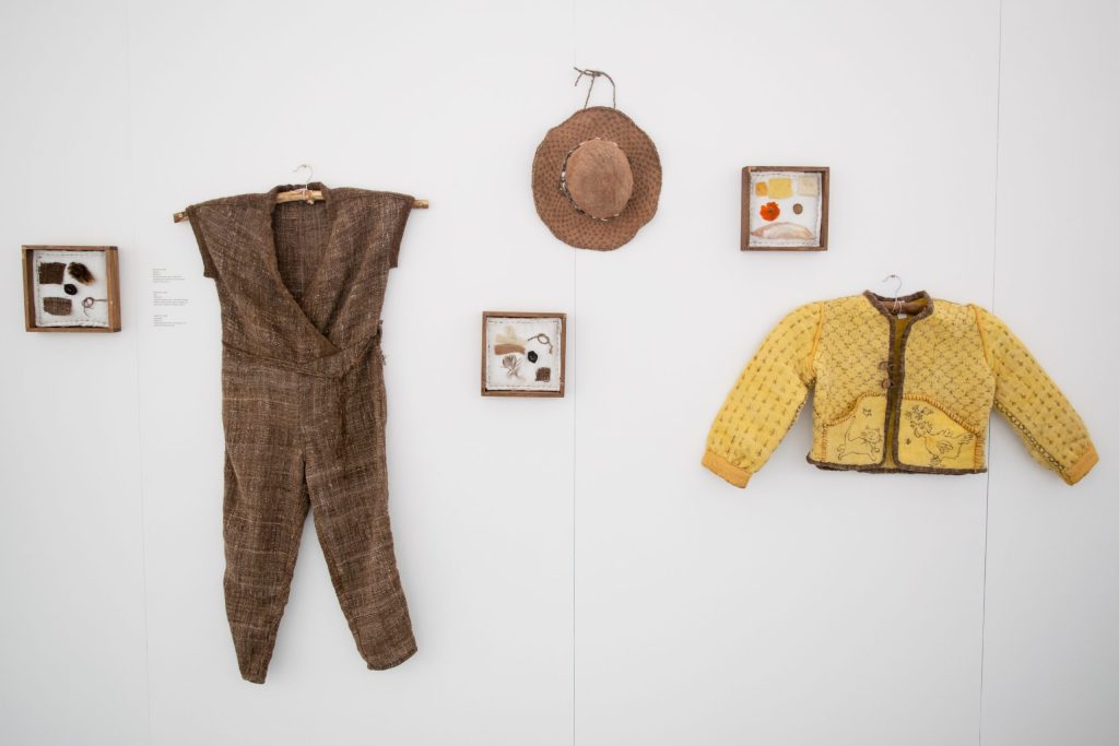 Image: An assemblage of clothes hang on the wall. One Year One Outfit participant Gretchen Graff’s outfit made entirely from fiber from her own animals and dyestuff she grew. Photo Courtesy of Rust Belt Fibershed.