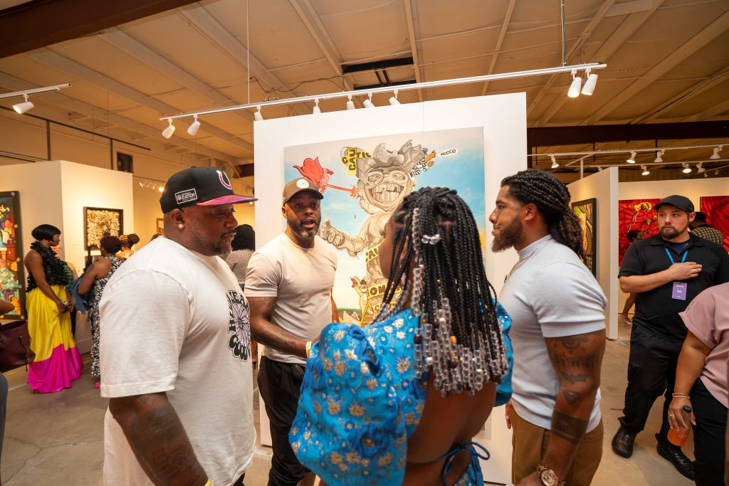 Image: Malina Simone and Alan Bacon at an art exhibition in conversation with other attendees. Image courtesy of GANGGANG.