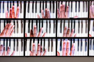 Close up video still of Paul Stephen Benjamin Sonata in Absolute Black All the Black Keys. The still shows twelve shots of Benjamin playing the black keys on different parts of the piano to make a song. Image by Colin Conces. Image courtesy of Bemis Center.