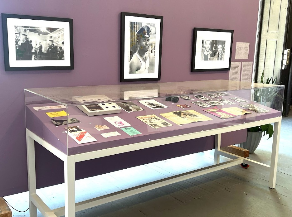 Image: Installation view of Just Below the Surface. An archival collection displayed at the exhibition, containing archival materials such as Gay Chicago Magazine, other ephemera, and photographs by Solís and McCoy on the wall. Photo courtesy of Chicago Art Department.