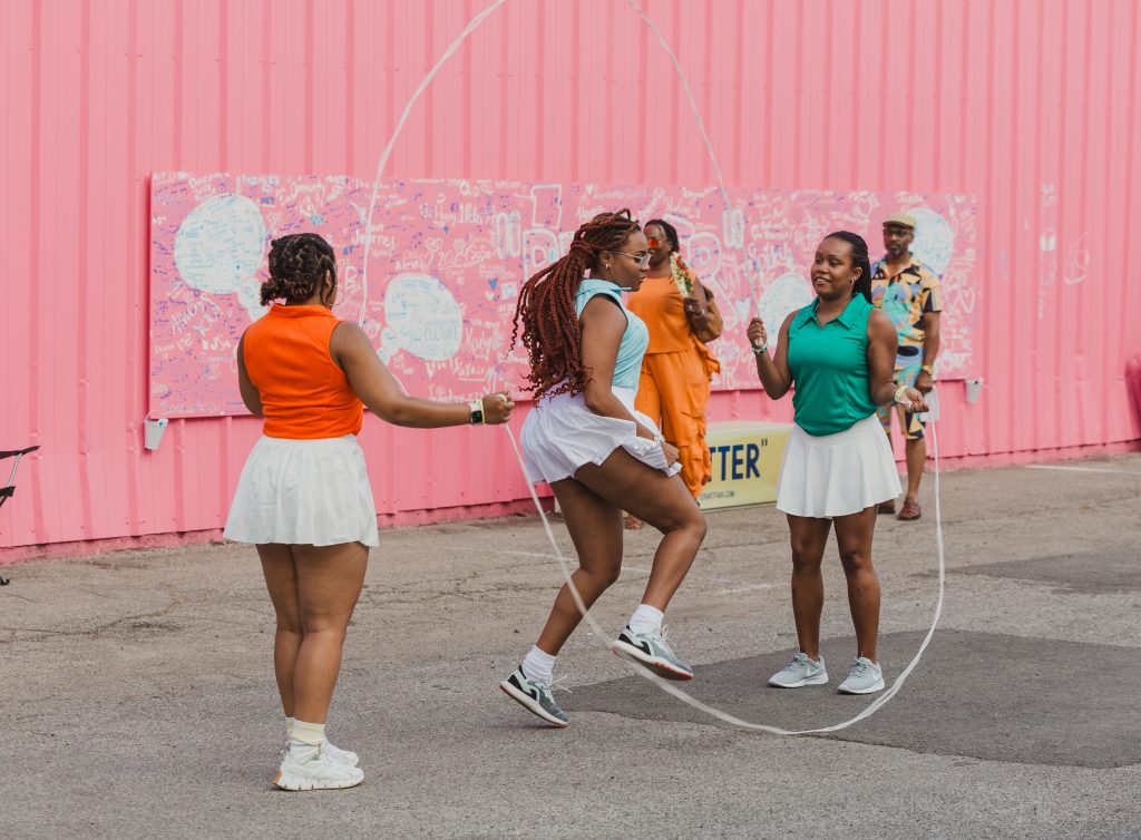 Image: Three young people jumping double dutch in front of the BUTTER signage. The building behind them is bright pink. Image courtesy of GANGGANG.