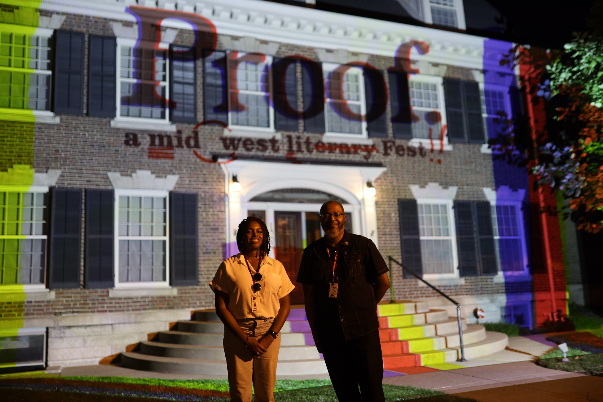 Image: Chantel Massey & Mitchell L. H. Douglas standing in front of a building with the words "Proof: A Midwest Lit Fest" projected onto it. Photo credit: Indiana Humanities.