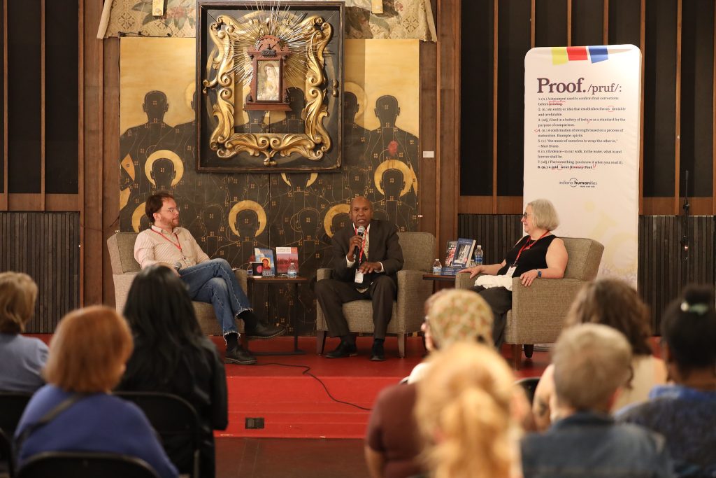 Image: At Proof: A Midwest Lit Fest, a crowd of people listen to the panel discussion You Can’t Go Home Again with novelist and longtime New York Review of Books contributor Darryl Pinckney and Indiana Authors Award Lifetime Achievement winner Susan Neville. On the left sits moderator Taylor Lewandowski, owner of Dream Palace Books. In the center sits author Darryl Pinckney. On the right sits author Susan Neville. Photo credit: Indiana Humanities.