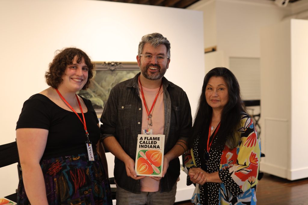 Image: At Proof: A Midwest Lit Fest, a reading by A Flame Called Indiana anthology contributors: (left) poet Sam Fain, (center): poet Doug Paul Case, editor, A Flame Called Indiana, (right): poet Nancy Chen Long. Doug Paul Case holds a copy of A Flame Called Indiana towards the camera. Photo credit: Indiana Humanities