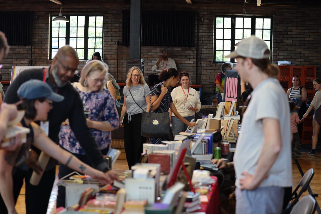 Image: A crowd of people peruse the different tables of books at Proof: A Midwest Lit Fest in Indianapolis, IN. Photo credit: Indiana Humanities. 