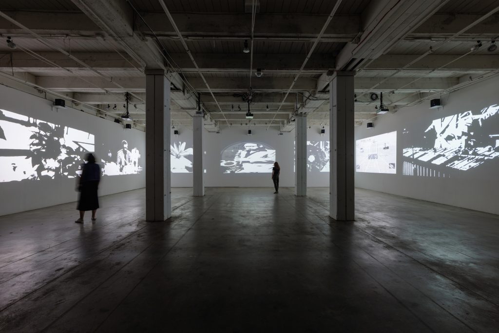 Image: An installation view of Black Prairie Septet by Paul Stephen Benjamin, as part of his solo exhibition Black of Night at Bemis Center. The photo shows three of the four walls of a large gallery space. Each wall has several black and white photos of images on it, mostly of Jazz musicians. Photo by Colin Conces, courtesy of Bemis Center.