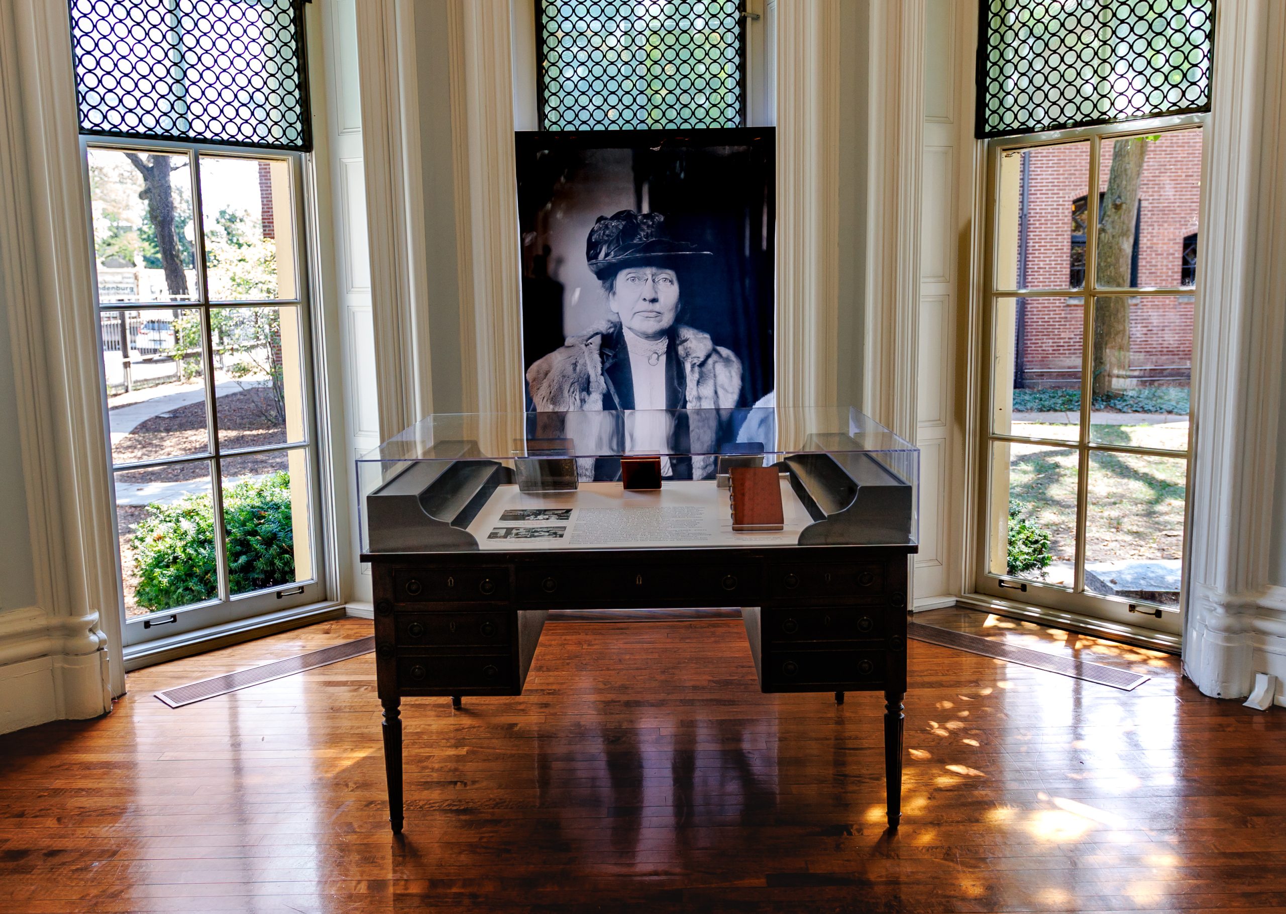 Image: A photo of the rotunda at the Hull-House Museum. A selection of books bound at Hull House are displayed in front of Ellen Gates Starr’s portrait. Photographed by Sarah Larson. The portrait depicts Starr under arrest during the Henrici restaurant waitress strike, 1914. Chicago Daily News Photograph Collection, Chicago History Museum. DN-0062288.