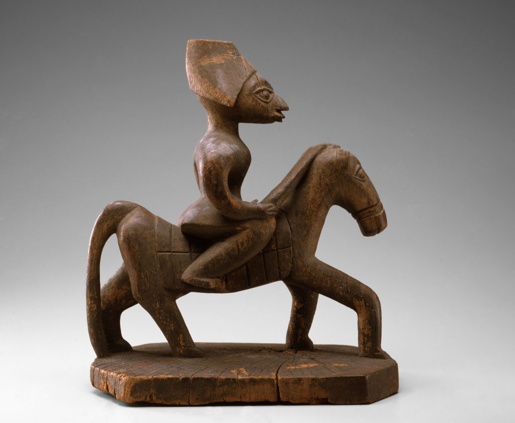 Image: Yoruba Peoples, Republic of Benin Horse and Rider, early 20th century, Carved wood. A wood sculpture of a man with a headdress riding a horse positioned on a plinth. Image courtesy of Toledo Museum of Art.