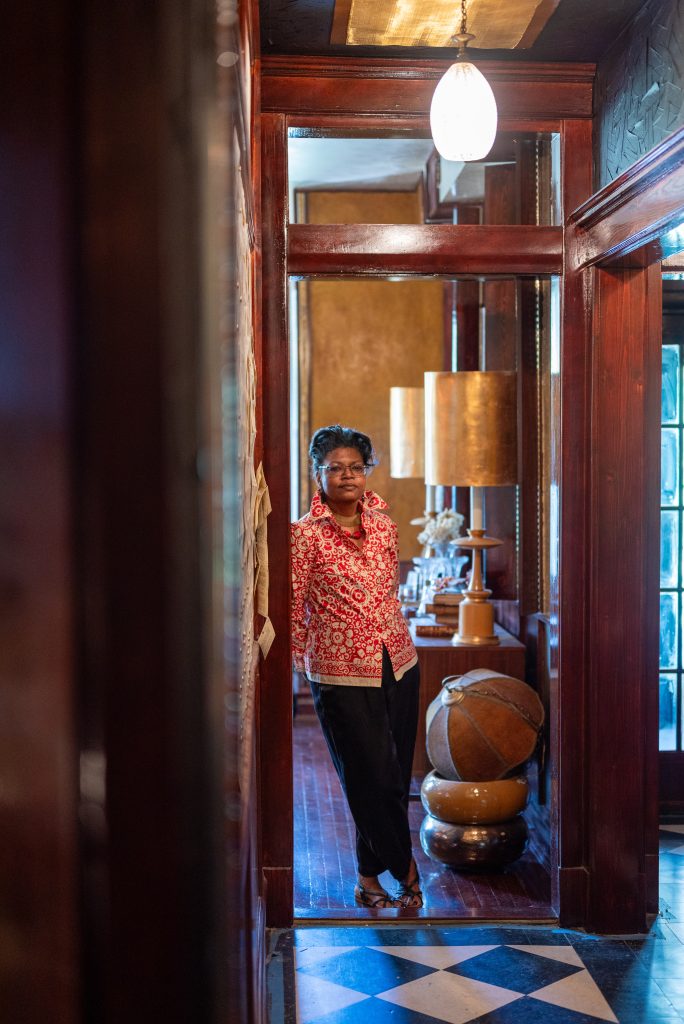 Center Image: A portrait of Clemenstein Love in the doorway of the Greystone Studio and Home. She is leaning against a wall with her hands behind her back and her legs crossed at the ankles. She looks directly at the camera. Photography by Tonal Simmons.