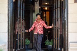 Image: Clemenstein Love stands in The Greystone looking outside through open french doors. Her hands are on each of the doors as she looks outside with purpose. Photograph by Tonal Simmons.