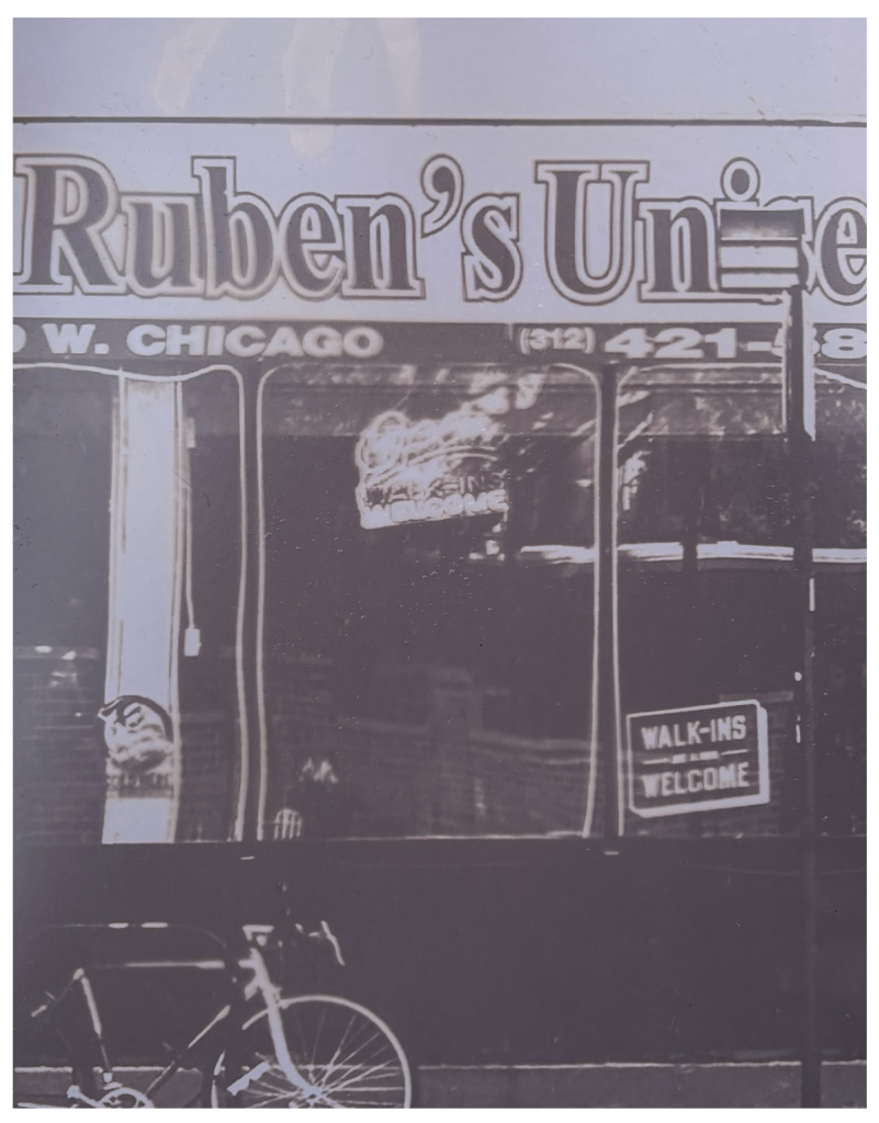 Image: At the bottom left of the image is a bicycle tied to a rack, standing in front of a window front with an awning that reads “Ruben’s” in a bold, outlined font, standing dark against the pale purple shade of the draping. The address and phone number to the business stands proudly on the lip of the awning in a thick, no nonsense font. Toward the bottom right is a sign that reads “Walk-ins welcome” in a purposely haphazardly, upward tilted direction that communicates a genuine sense of openness.