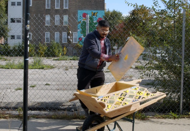 Imagen: Porta(til) Performance, foto del vídeo de Ruby Que. Carlos Flores frente a un terreno baldío, trabajando con una carretilla construida por el mismo. Cortesía del curador.