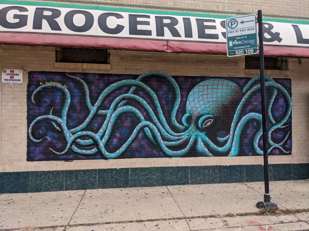 Image: Mural outside of an Albany Park grocery store by Natalia Virafuentes featuring blue and pink octopus in a sea of dark pink, blue and purple hues. Image by Natalia Virafuentes.