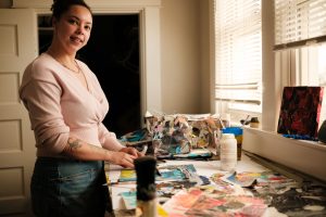 Image: Harriet Watson poses in front of the desk where she works on collages in her studio. Image by Seed Lynn.