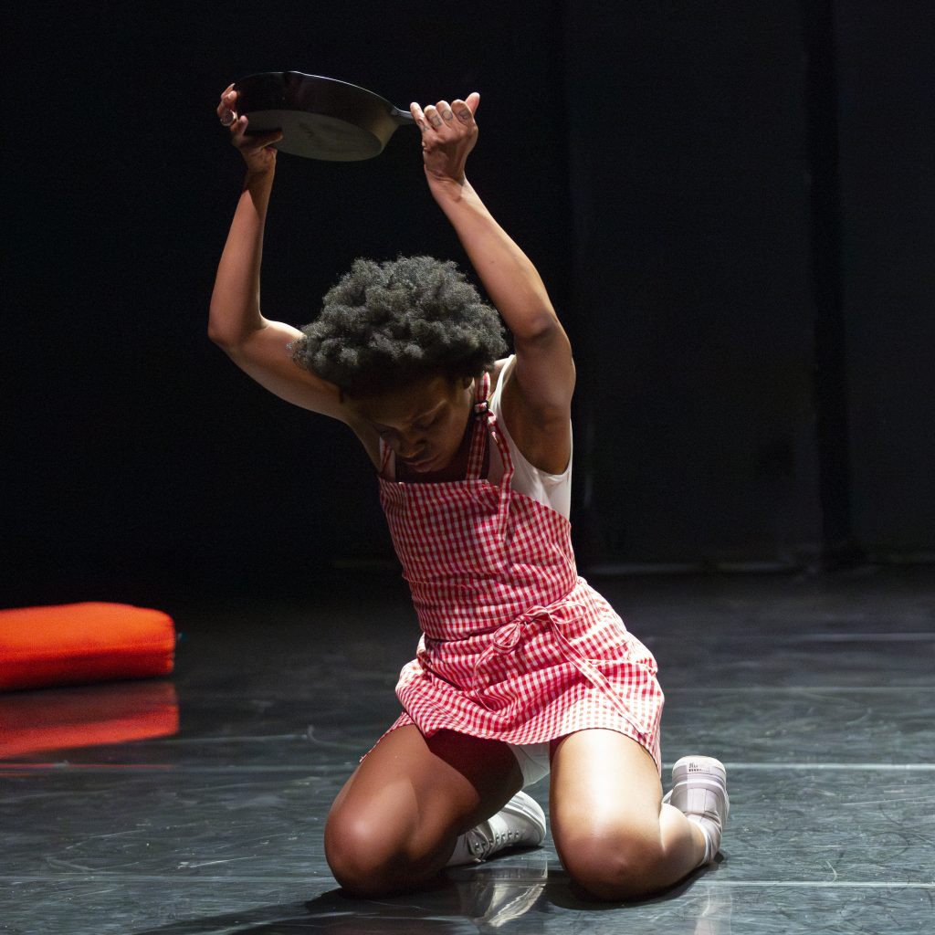 Image: Freeman | Po'Chop squats to bring the pan she used to cook food onto the stage floor. Photo by Natasha Moustache.