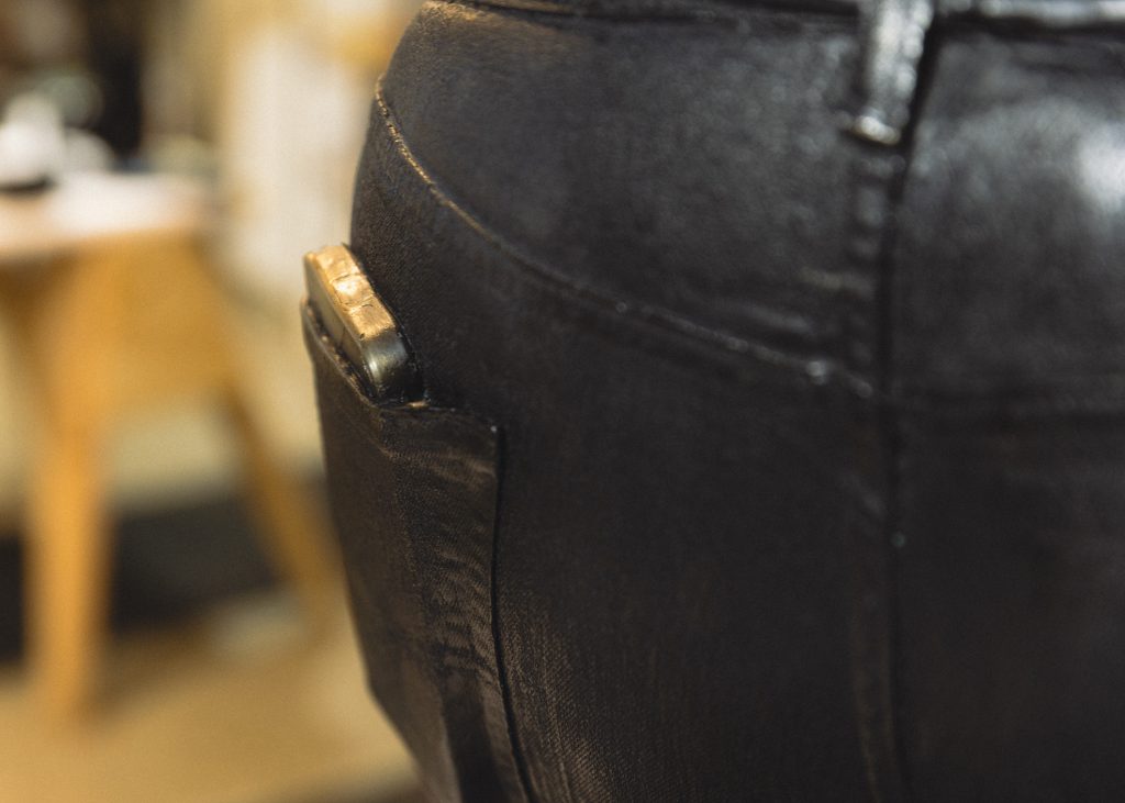 Image: A close-up detail of a bronze sculpture depicting a disembodied waist with jean pockets that holds a cellphone. Photo by Asa Featherstone, IV.