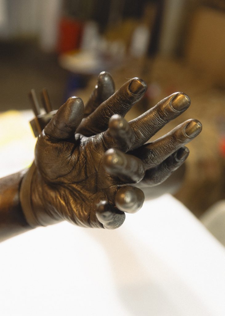 Image: A detail of a bronze sculpture depicting a pair of hyper-realistic hands detained by zip ties. Photo by Asa Featherstone, IV.