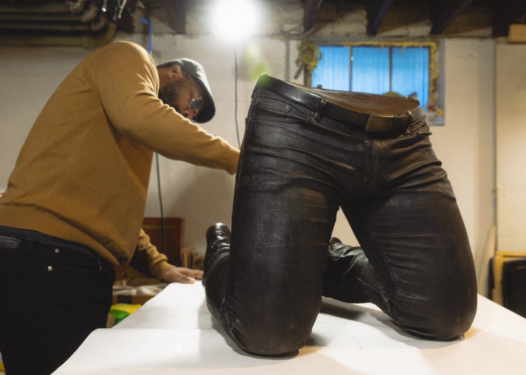 Image: Candid image of Michael Coppage in his studio handling his bronze sculpture that depicts a pair of disembodied knees and waist kneeling. Photo by Asa Featherstone, IV.