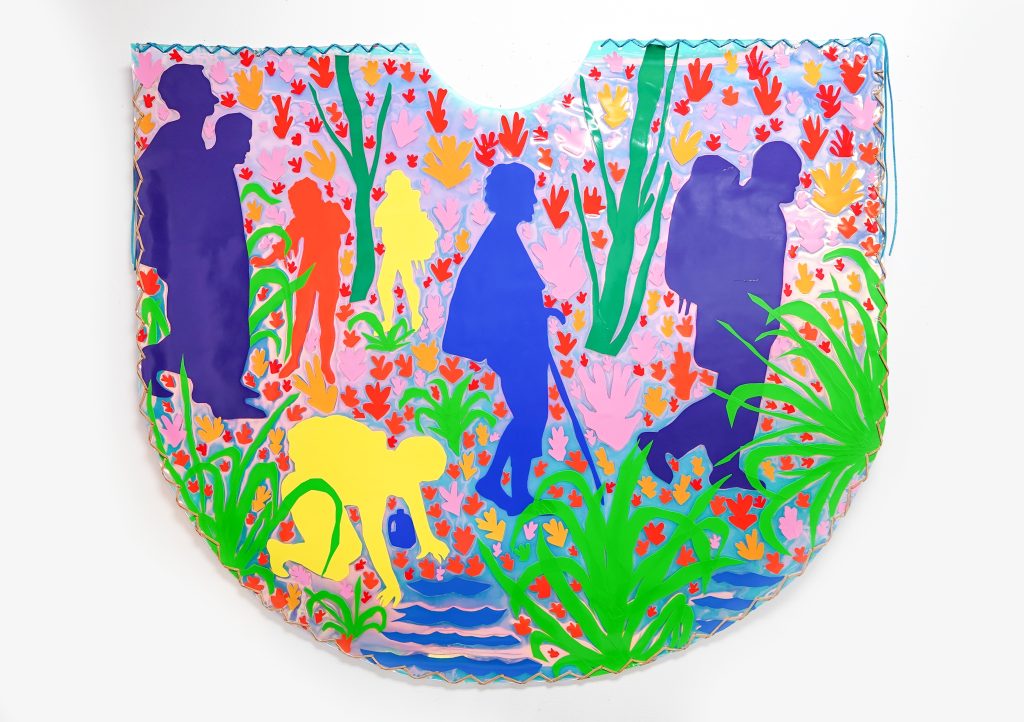 Image: Hoesy Corona. Climate Poncho 1, 2023. Courtesy of the artist. The colorful piece is slightly in the sape of a "U" and hangs on a white wall. The piece depicts silhouettes of figures walking across flora and tress, with one figure bending down towards water.