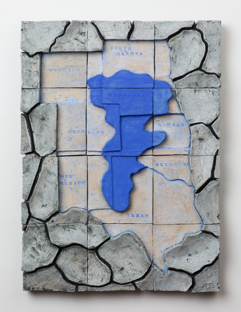 Image: Jess Benjamin. Dried Up On The Ogallala Aquifer 1-25. Photography by Colin Conces. Courtesy of the artist. A water-like, blue shape sits in a section of a United States map. Surrounding the map are rock-like forms.