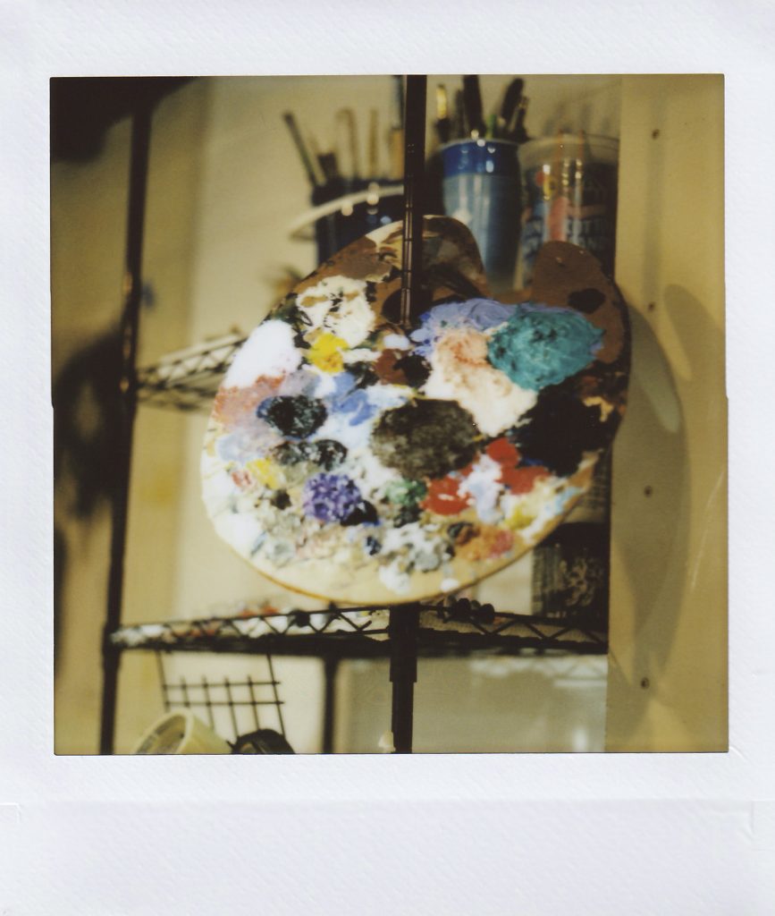 Image: Polaroid of a painter's palette covered with various paints, resting on a shelf. Photo by Asa Featherstone, IV.