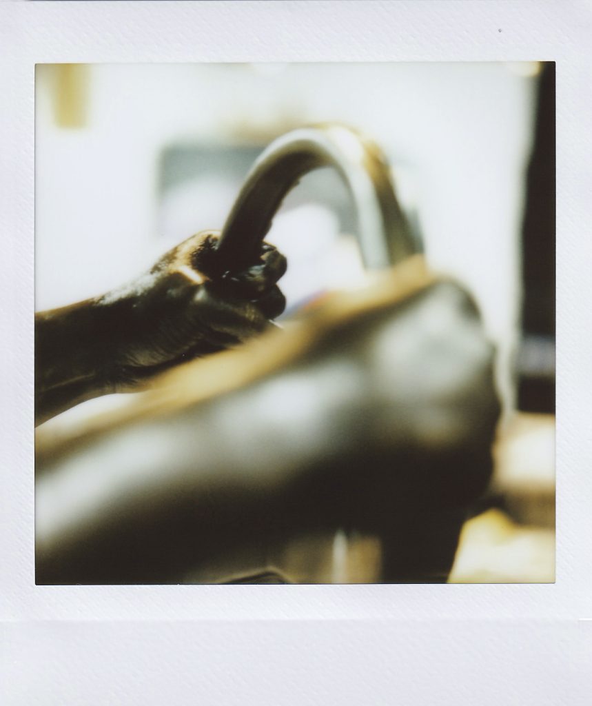 Image: Polaroid detail of a bronze sculpture depicting a pair of hands gripping a steering wheel. Photo by Asa Featherstone, IV.
