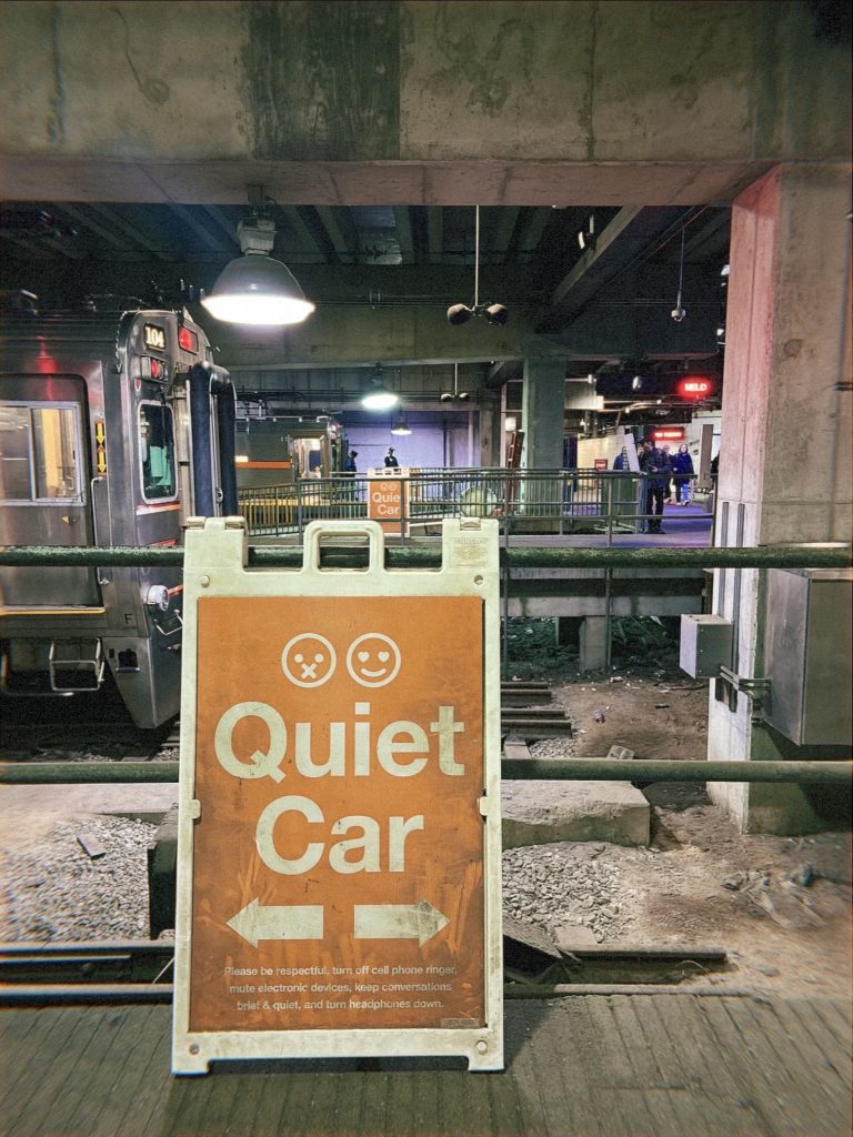 Image: Orange and white "Quiet Car" sign is shown leaning on the railing in front of a the pedway's many tracks. Image by Livy Snyder.