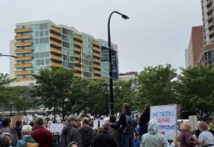 Image: People gathered in downtown Evanston mostly facing away from the camera and holding signs for the No Kings Rally. One sign says, "We The People Support Immigrants." Image courtesy of the author.