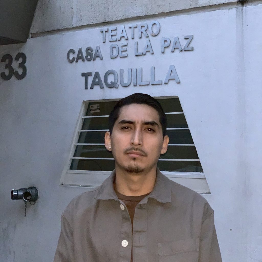 Image: A photo of Chuquimarca organizer, John H. Guevara, who looks straight at the camera. Behind them is a wall with the words: "TEATRO CASA DE LA PAZ / TAQUILLA". Image courtesy of the artist.