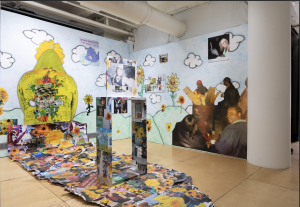 Image: Installation view of IJBOL fields. A wall with illustrations of clouds and sunflowers with photo transfer elements. Dante Moore, Self portrait with sunflower installation (detail), 2025, airbrushed ink, inkjet print on photo tex, inkjet print on bond, repurposed advertisement board, wood, solvent transfer, wheatpaste. Image courtesy of the artist.