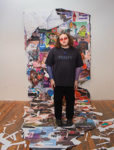 Image: Dante Moore in front of their large collage of photos with paper clippings on the ground. The artist wears two hair clips on each side of their curly hair, red shades, and a black shirt that reads "Trinity." Image courtesy of the artist.