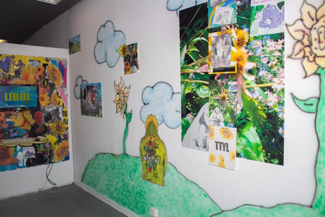 Image: Installation View, IBOL Fields (detail), 2025, at Happy Gallery Chicago. Airbrushed ink, inkjet print on photo tex, inkjet print on bond, repurposed advertisement board, and interactive unity 3D Game form a colorful installation on the wall. Image courtesy of the artist.