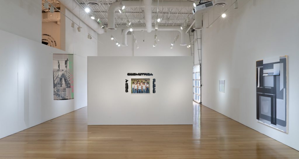 Image: Installation view of the Geometrica Pop Y Rucas at the gallery entrance, showing Jaasiel Duarte-Terrazas’s printed silk curtain (Curtain #1) hanging on the left, a group portrait by Evie Lozano and Brayan Enriquez (Poder En Unidad (Formación No. 1)) in the center wall, and Caleb Taylor’s Articulation 03 acrylic painting on the wall to the right. Photo courtesy of Charlotte Street Foundation.