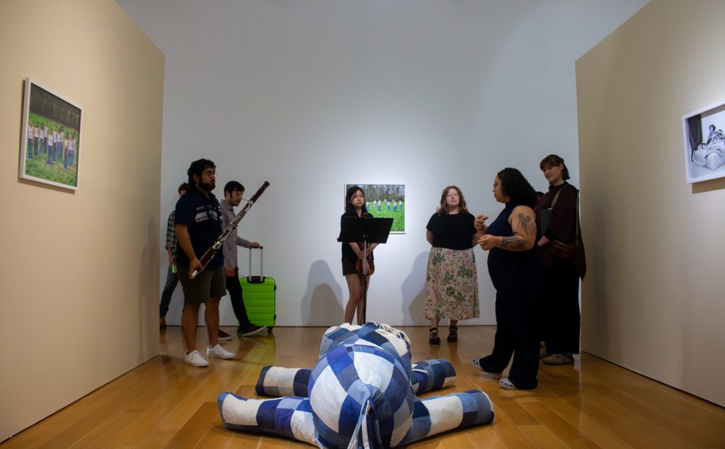 Image: Yashi Davalos, the curator of Geometrica Pop Y Rucas, speaking to the musicians in front of Gabriella Poulos’s denim horse sculpture (Miles To Go #1) during rehearsal. Photo courtesy of Charlotte Street Foundation.