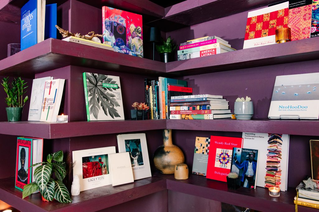 Image: A photograph of Chuquimarca’s art book collection on a dark purple shelf at Tala Gallery. Photo courtesy of Tala Gallery. Photographer: Steven Piper.