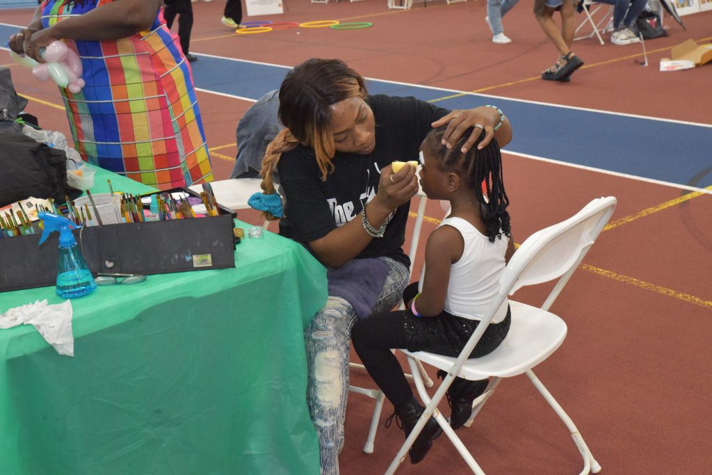 Image: A young girl sits in a chair as an woman paints her face during the Wonder of Words Festival. Image by Edvétte Wilson Jones.