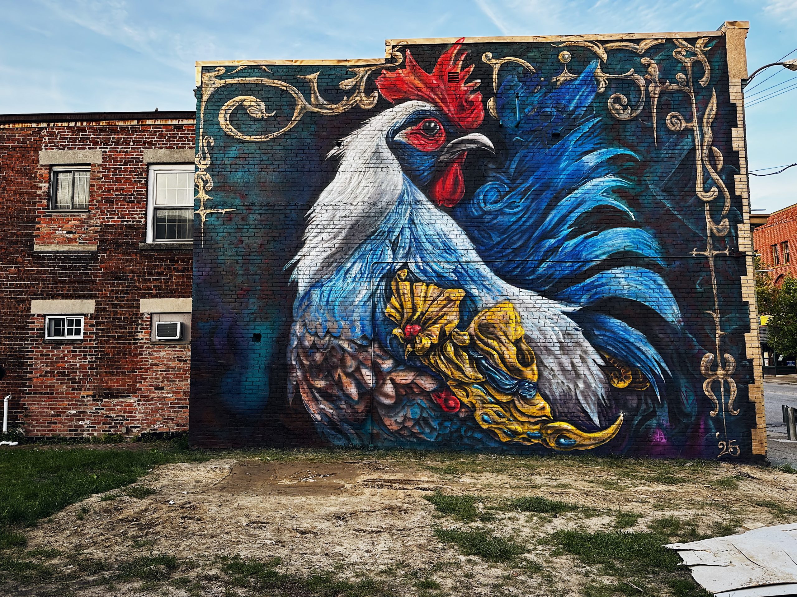 Image: a mural of a rooster on a navy background with an ornate golden frame. The rooster has a golden wing with encrusted jewels. Image by Coly Puzzouli.