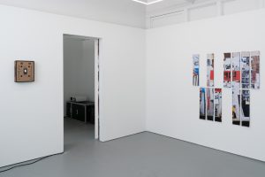 Image: Installation view of a corner of the gallery. On the left, the artwork Speech Assistance Machine (Leonard Cohen’s Democracy, 1992). Materials include a Fruit shipping box, 3.2-inch Raspberry Pi LCD screen, birch plywood frame, and video. On the right, is an artwork titled Self-portrait as a table. It includes eleven printed photographs on twenty layers of upcycled posters. Image courtesy of Letters to Nora.