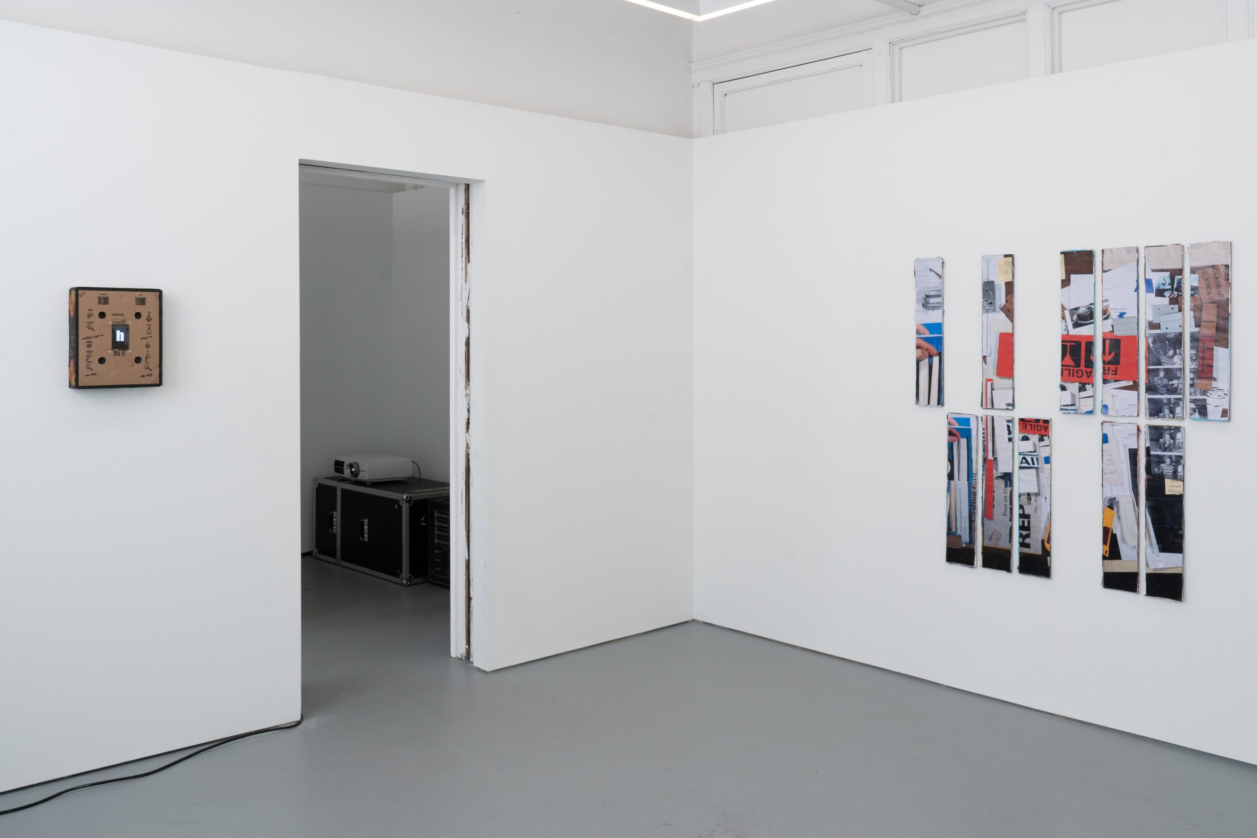 Image: Installation view of a corner of the gallery. On the left, the artwork Speech Assistance Machine (Leonard Cohen’s Democracy, 1992). Materials include a Fruit shipping box, 3.2-inch Raspberry Pi LCD screen, birch plywood frame, and video. On the right, is an artwork titled Self-portrait as a table. It includes eleven printed photographs on twenty layers of upcycled posters. Image courtesy of Letters to Nora.