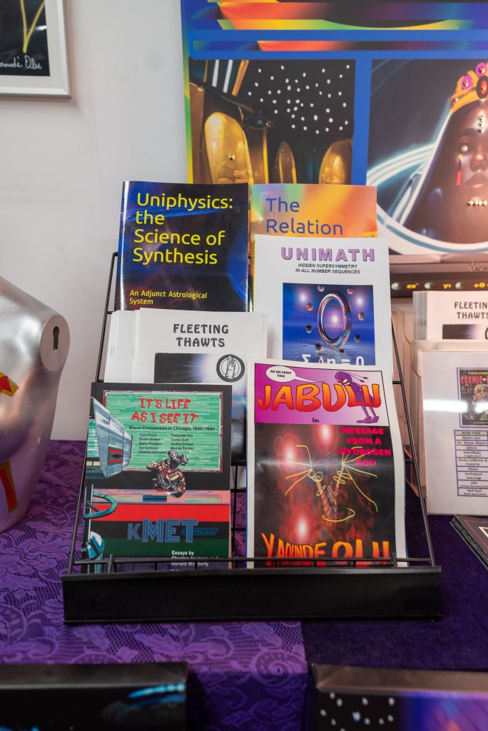 Image: Uniphysics: the Science fo Synthesis, Jabulu, Unimath by Olu and "It's Life as I See It', which features Olu's work are shown displayed on a magazine rack on a table in Olu's showroom. Image by Tonal Simmons.