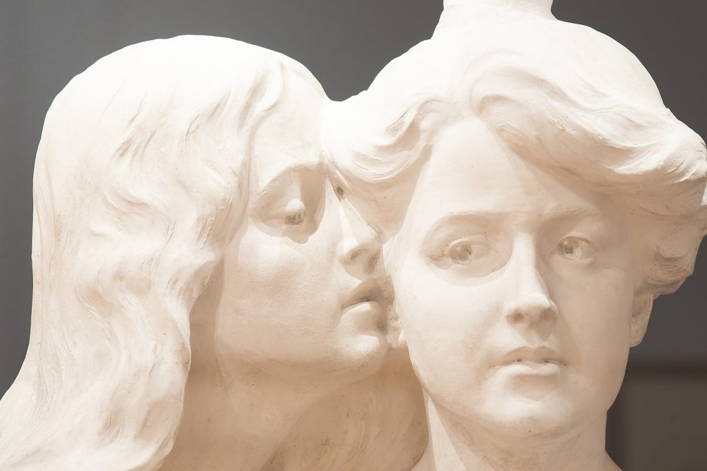 Image: Installation view of “The First Homosexuals: The Birth of a New Identity, 1869–1939,” at Wrightwood 659, 2025. A sculpture of a woman with long hair whispers into the ear of a woman with an updo. Photo courtesy of Daniel Eggert (@DesigningDan).