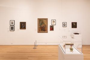 Image: Installation view of "The First Homosexuals: The Birth of a New Identity, 1869-1939," at Wrightwood 659, 2025. Seven portraits hung on a white wall behind stanchions, and two works in vitrines. Photo courtesy of Daniel Eggert (@DesigningDan).