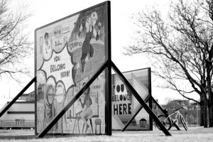 Image: “You Belong Here” by Laura Gomel (foreground) and Brett Whitacre (background), photograph by Alan León. A black and white photograph of two billboard-sized signs that each say “YOU BELONG HERE”. Courtesy of Belt Publishing.