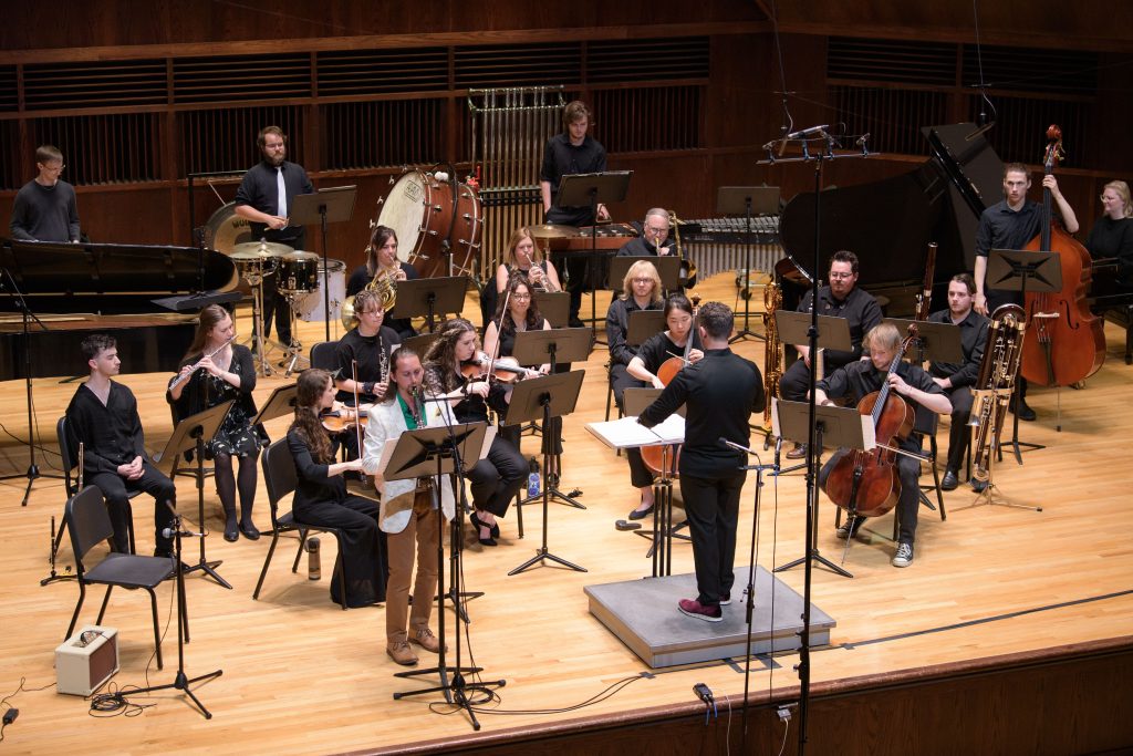 Image: The Sound Ecologies Chamber Orchestra on stage with conductor Elliott Lentz and clarinet soloist Eric Salazar performing "Concertino Espresso" by Luke Garrigus. Image courtesy of Sound Ecologies.