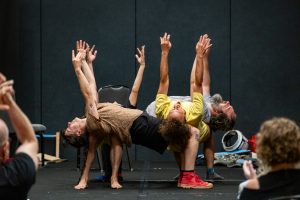 Four performers dance onstage as part of the 2025 Socialism Conference at Chicago's McCormick Place convention center. The four performers are bending at the knee while balancing with their backs resting in each other's lap with their arms raised into the air.
