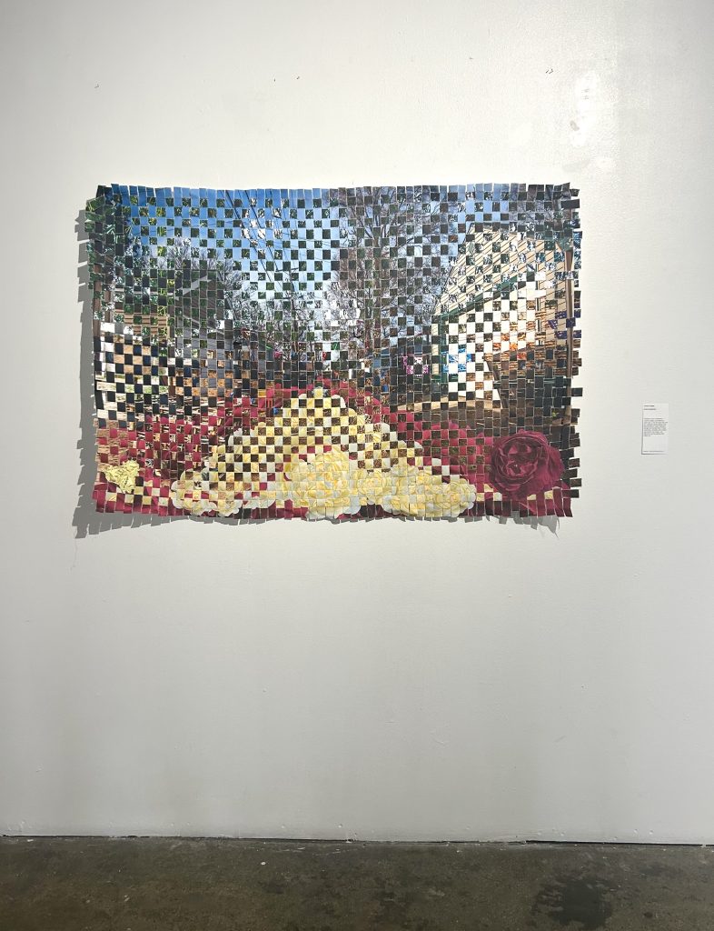 Image: Installation view from We Built This: Making Through Migration. Entre Espacios by Carina Yepez hangs on a white gallery wall. The artwork is a blend of two images woven together. It depicts floral imagery, blending urban and organic landscapes. Image courtesy of Zhou B Art Center.