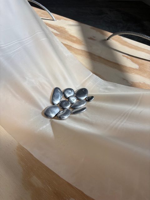 Close up photo of the piece stone babies, which sits upon The material plane. Both pieces are by bex ya yolk. stone babies appears as a collection of metallic stones cradled together. Photo courtesy of Chicago Artists Coalition.