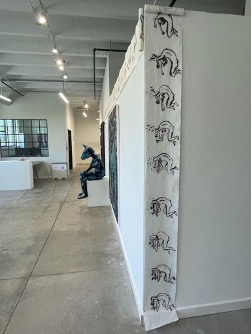 Cecilia Beaven, Unbroken (Scroll), 2025. Ink on rice paper scrolls, 11”x80’. The corner of a gallery wall is draped from top to bottom with a scroll of paper containing ink drawings. Photo courtesy of the curator.
