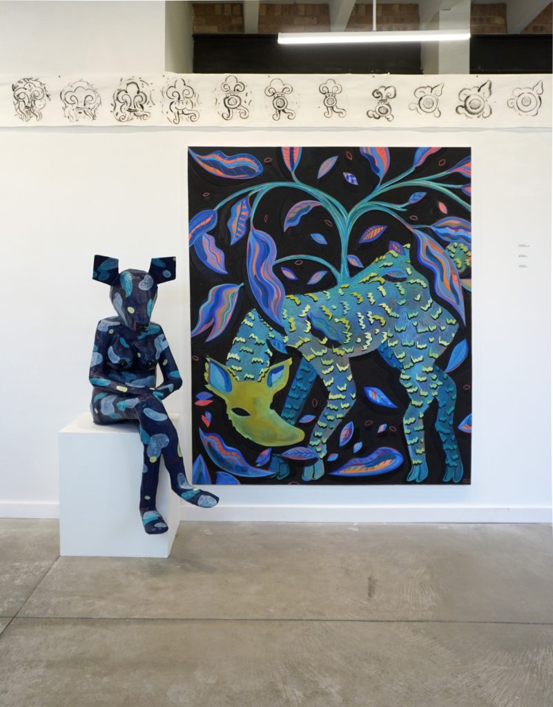 Three works by Cecilia Beaven are on display (clockwise from the top): Unbroken (Scroll), 2025, ink on rice paper scrolls, 11”x80’; Lean Down, 2025, acrylic and oil on canvas, 72”x60”; and Mujer Venado, 2025, paper mache and acrylic, 55”x18”x36”. A gallery wall with an ink drawn scroll across the top. Centered is a life-size paper mache sculpture sitting next to an acrylic and oil painting. Photo courtesy of Chicago Artists Coalition. 