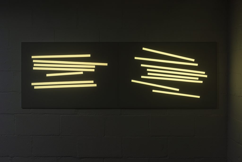 A 35mm projection of more than a dozen rectangles of yellow light arranged in two uneven columns.